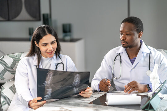 Two professional doctors discussing an x-ray result together in a modern clinic office, analyzing medical data for diagnosis and patient treatment with professional healthcare collaboration.