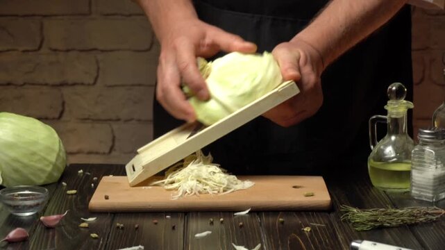 A chef skillfully slices fresh cabbage using a mandoline on a wooden cutting board. The kitchen is neatly arranged with ingredients and tools nearby.