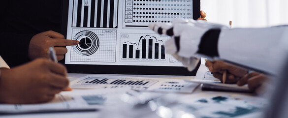 A diverse group of professionals engages in a collaborative analysis of data trends on a tablet. They highlight key performance metrics in a modern office environment.Noogenesis