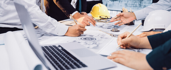 A diverse team of engineers and architects collaborates on project plans in a modern office setting, surrounded by construction tools and documents, emphasizing teamwork. SACTR