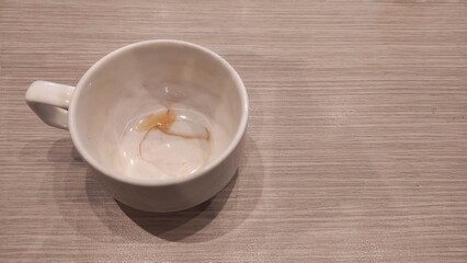 An empty white cup sits on a light wooden surface, showing faint tea stains inside that suggest a recently finished drink and a quiet, simple moment.