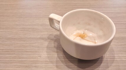 An empty white cup sits on a light wooden surface, showing faint tea stains inside that suggest a recently finished drink and a quiet, simple moment.