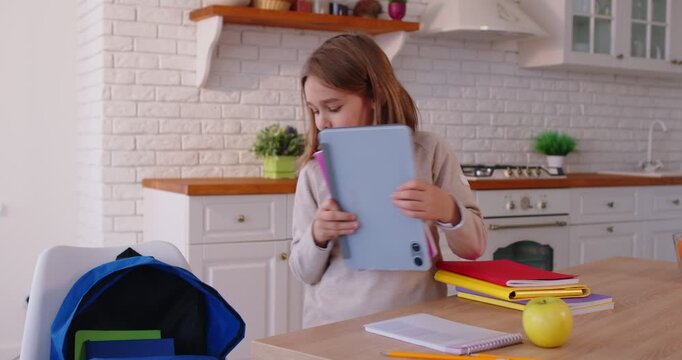 Cheerful school child packing colorful notebooks into backpack on kitchen table, preparing for school day. Focused young pupil organizing study materials and supplies before going to school.