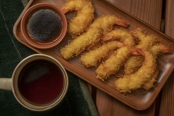 Crispy tempura shrimp served on wooden platter with dipping sauce and tea, perfect for sharing