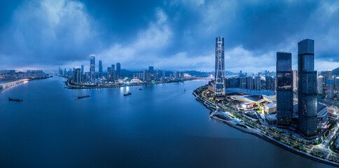 Fototapeta premium Panoramic view of a modern waterfront city skyline with illuminated buildings and reflection in the water during blue hour in Zhuhai.