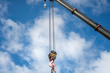 Obraz premium Crane machinery is lifting heavy object using the spreader bar on cloudy sky background. Industrial operation scene and equipment object.