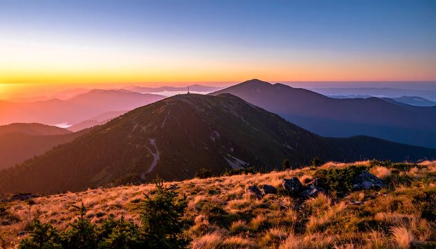 A scenic vista of a mountain range at dawn, with vibrant orange and purple hues. The foreground features grassy terrain