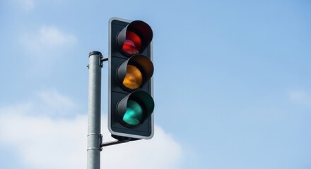A traffic light with red, yellow, and green lights illuminated against a clear blue sky.