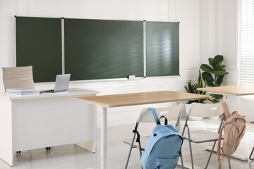 Green chalkboard, backpacks and stylish furniture in classroom. Mockup for design