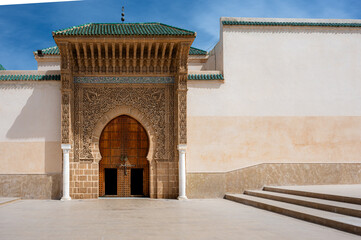 Wide shot of the ornate entrance to the Mausoleum of Moulay Ismail in Meknes, Morocco, showcasing intricate tilework, carved arches, and geometric patterns under clear daylight.

