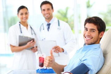 A cheerful young man donating blood in a clinic, surrounded by supportive medical staff. The atmosphere is positive and encouraging, promoting health awareness.