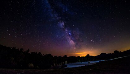 Stunning nightscape. The vibrant Milky Way galaxy arches across a deep blue sky, with a forest below silhouetted against the horizon