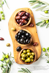 Olives in wooden bowls and Olive oil in the bottle at white table.