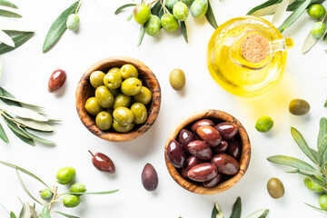Olives in wooden bowls and Olive oil in the bottle at white table.