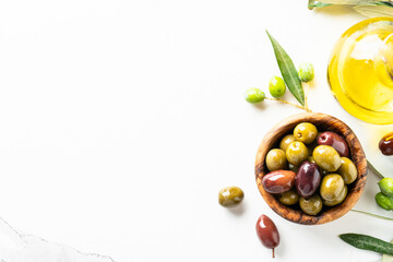 Olives in wooden bowl and fresh olive tree branch at black background.