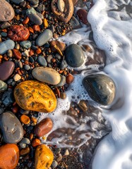 Colorful beach pebbles nestled on wet sand, partially submerged by foamy ocean water