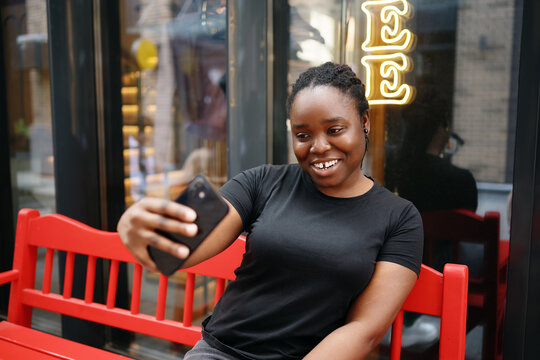 Smiling young woman creating content and taking selfie with smartphone outdoors in the city. Concept of digital communication, blogging, and modern urban lifestyle.