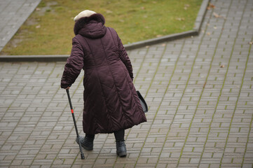 An elderly woman walking alone with a cane on the street