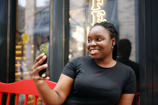 Smiling young woman creating content and taking selfie with smartphone outdoors in the city. Concept of digital communication, blogging, and modern urban lifestyle. - Powered by Adobe