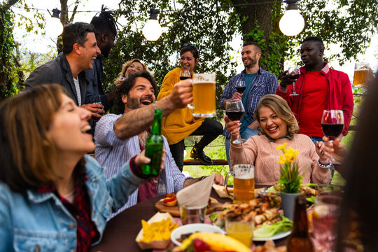 happy people toasting drink glasses sitting bar table – friends toasting red wine and beer on rooftop dinner party – food and beverage life style concept