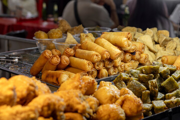 A vibrant display of various fried street food items, including golden spring rolls and crispy snacks, at a bustling night market in Bangkok's Chinatown, offering a taste of local cuisine.