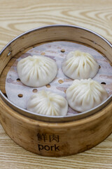 A bamboo steamer holds four freshly steamed pork soup dumplings, also known as Xiao Long Bao, ready to be enjoyed. This popular Chinese delicacy is a must-try at any night market or Chinatown.