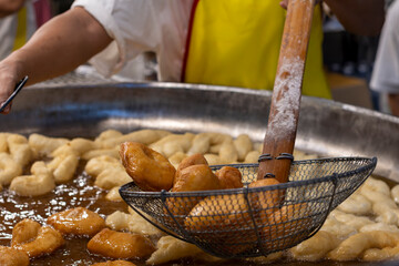 A street food vendor expertly deep-fries golden-brown dough fritters in a large pan, a popular sight and smell at bustling night markets in Bangkok's vibrant Chinatown.