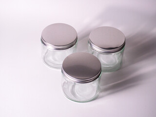Three clear glass jars with silver lids arranged on a clean white surface, perfect for product packaging, storage, or DIY projects.
