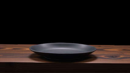 Black ceramic plate on wooden table with dark background, simple and elegant design for modern dining setting