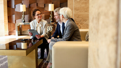 Business professionals meeting and discussing strategy using a digital tablet in a modern hotel lobby lounge area
