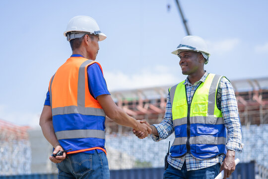 Diverse Construction Engineers Shaking Hands to Seal a Deal on Site, Two Happy Workers in Safety Gear Greeting Each Other with a Handshake.