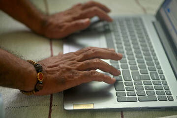Brown skinned man typing on a laptop.