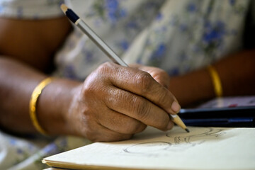 Close up of brown skinned woman's hand sketching with a wooden pencil on paper.