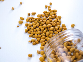 Delicious crunchy coated peanuts spill from a clear jar onto a clean white surface, perfect for snack advertising.