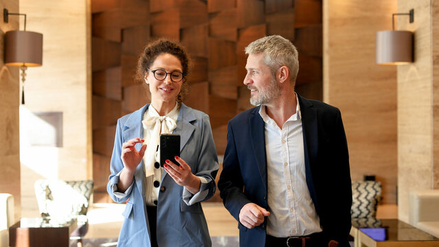 Business colleagues walking together in a modern office, woman showing information on smartphone to man