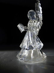 Sparkling crystal angel figurine holding a book, casting ethereal light in a dramatic dark studio setting, perfect for holiday decor and spiritual themes.