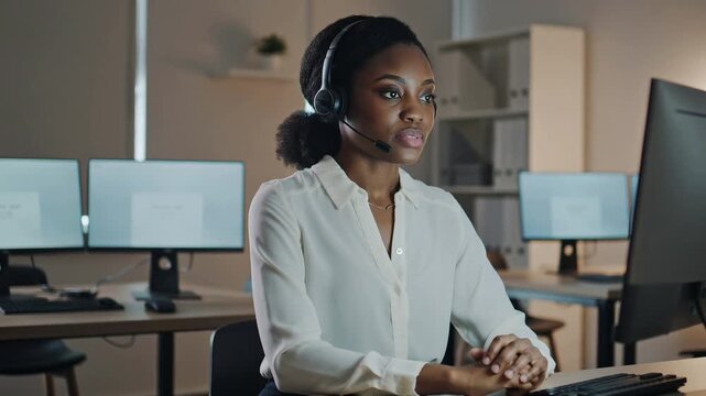 Black female call center agent sitting at her desk, wearing a professional headset, engaged in conversation with a customer