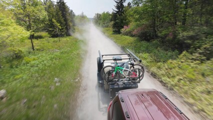 A teardrop camper trailer with bikes travels along a dusty road in Monongahela National Forest, surrounded by lush greenery and mountains during a peaceful camping trip.