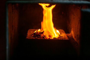 Flame in a pellet stove burner inside the combustion chamber, close-up heating process, bright fire and embers in a home boiler room