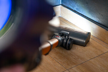 Vacuuming floor near baseboard with a cordless vacuum cleaner, cleaning head in motion, removing dust and dirt in a home interior.