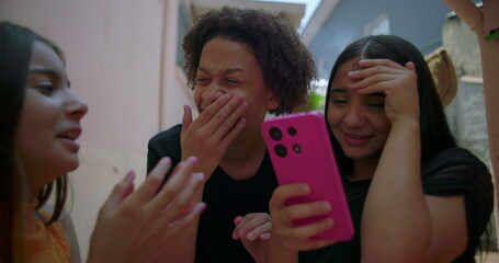 Teenagers reacting to social media post on smartphone in suburban alleyway, one girl showing...