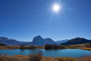 Lake Iman or Lech da Iman, a little mountain lake in alpine meadows of Puez-Odle Nature Park in Dolomites. An ideal rest area in a popular hiking to Seceda mount. Rays radiating from the sun.
