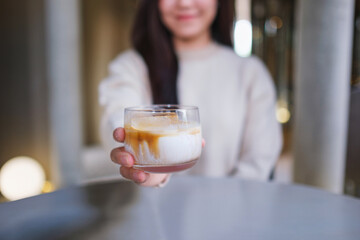 Closeup image of a woman holding and serving a glass of dirty coffee