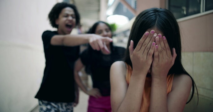 Teenager covering face in distress while friends laugh in suburban alleyway, representing youth bullying, peer relationships, and emotional challenges