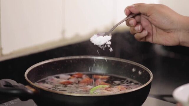 Adding salt with spoon while cooking in the kitchen.