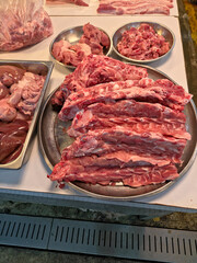 High-angle view of a market meat display, showing raw pork ribs on a round tray, surrounded by bowls of chopped meat and a pan of organs.