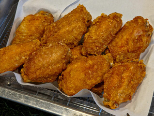 Overhead close-up of golden-brown fried chicken wings on white parchment paper in a clear or metal container.