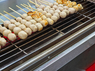 Row of skewered white pork meatballs grilling over charcoal, some starting to brown, typical of a street food snack.