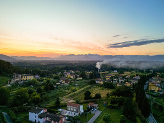 Aerial view of the Tuscan countryside during sunset, showing rustic village houses surrounded by...