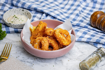 Crispy calamari rings arranged in a bowl, alongside lemon wedges and a dipping sauce